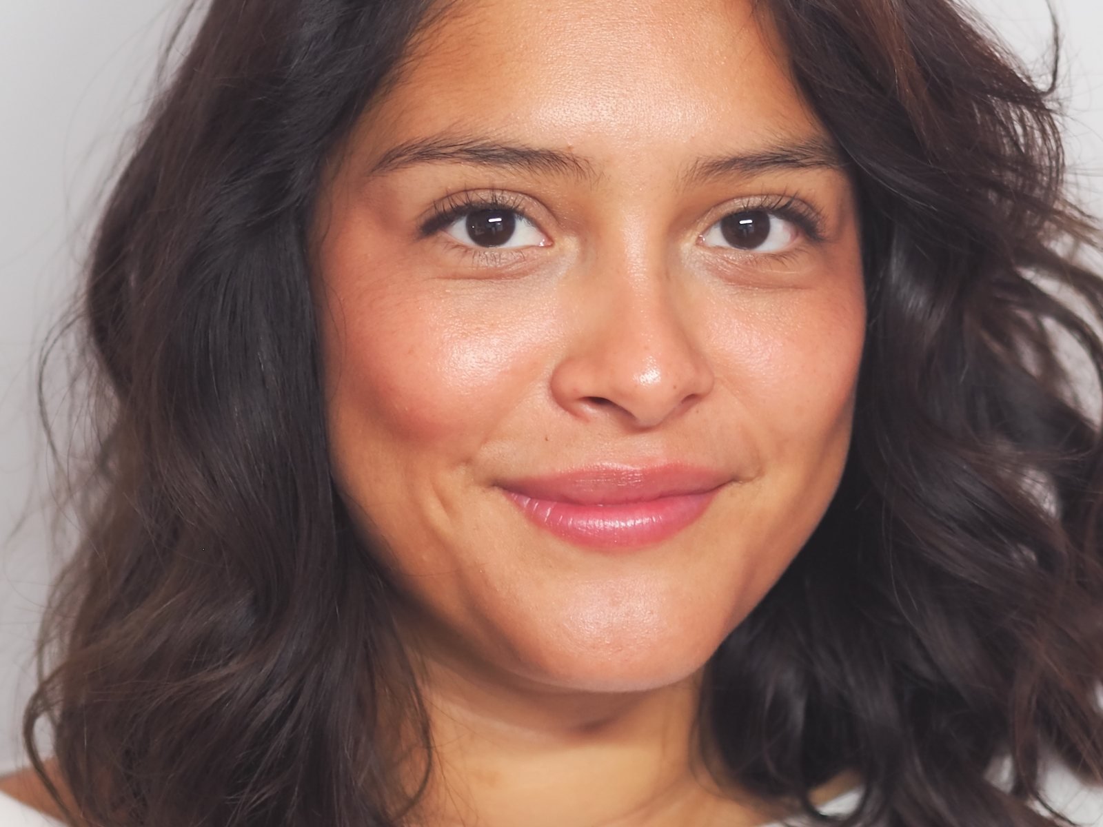 Visage de face, léger sourire, peau lumineuse, cheveux bruns ondulés
