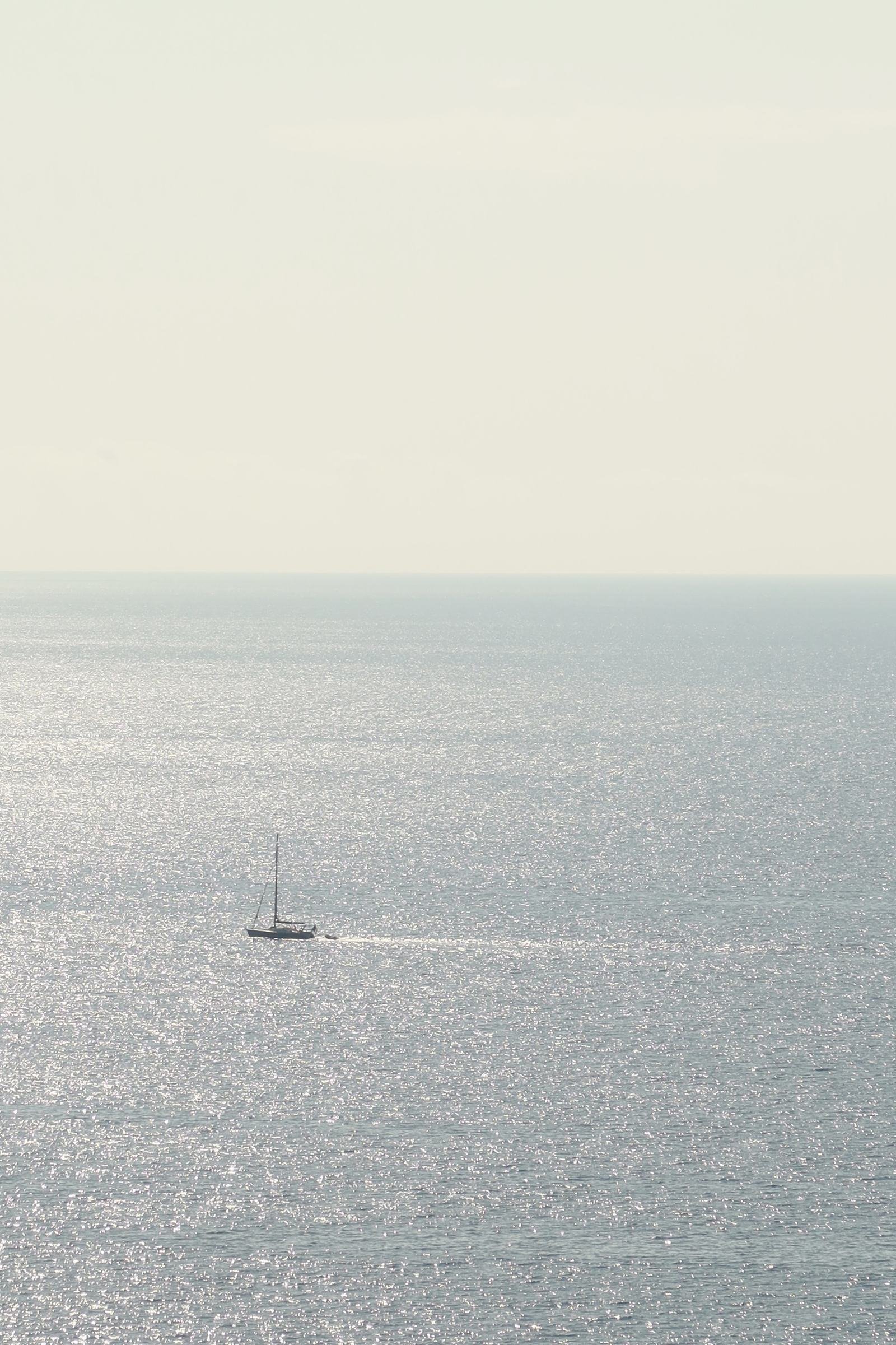 La mer à Cap-d’Ail sous un ciel blanc, un voilier à l’horizon, vue depuis chez moi
